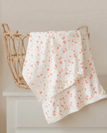 Floral-patterned towel draped over a wicker basket on a white surface.