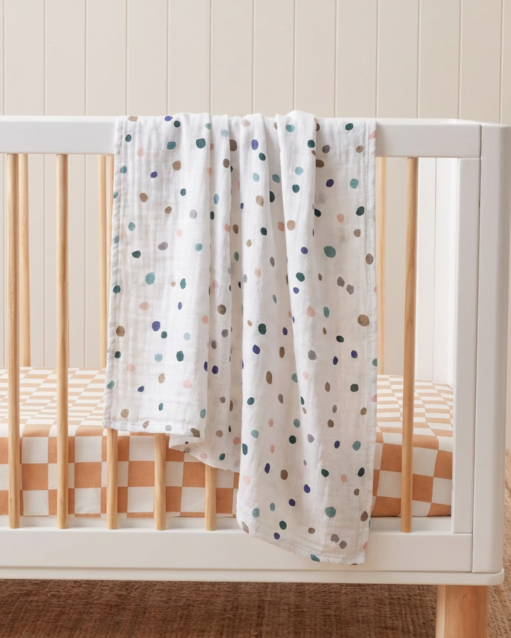 White crib with a polka dot blanket in a room with a wooden floor and white wall.