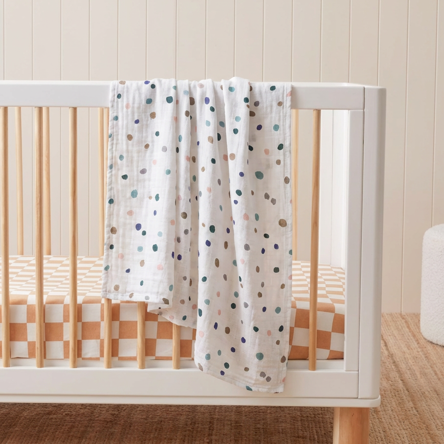White crib with a polka dot blanket in a room with a wooden floor and white wall.