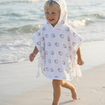 A young child walking barefoot on a sandy beach wearing a white hooded poncho with a black cartoon animal print.