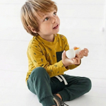 Child wearing a yellow shirt and green pants holding a white object on a white background