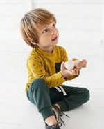 Child wearing a yellow shirt and green pants holding a white object on a white background