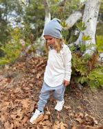 Child in a forest setting wearing a white jacket and gray beanie.