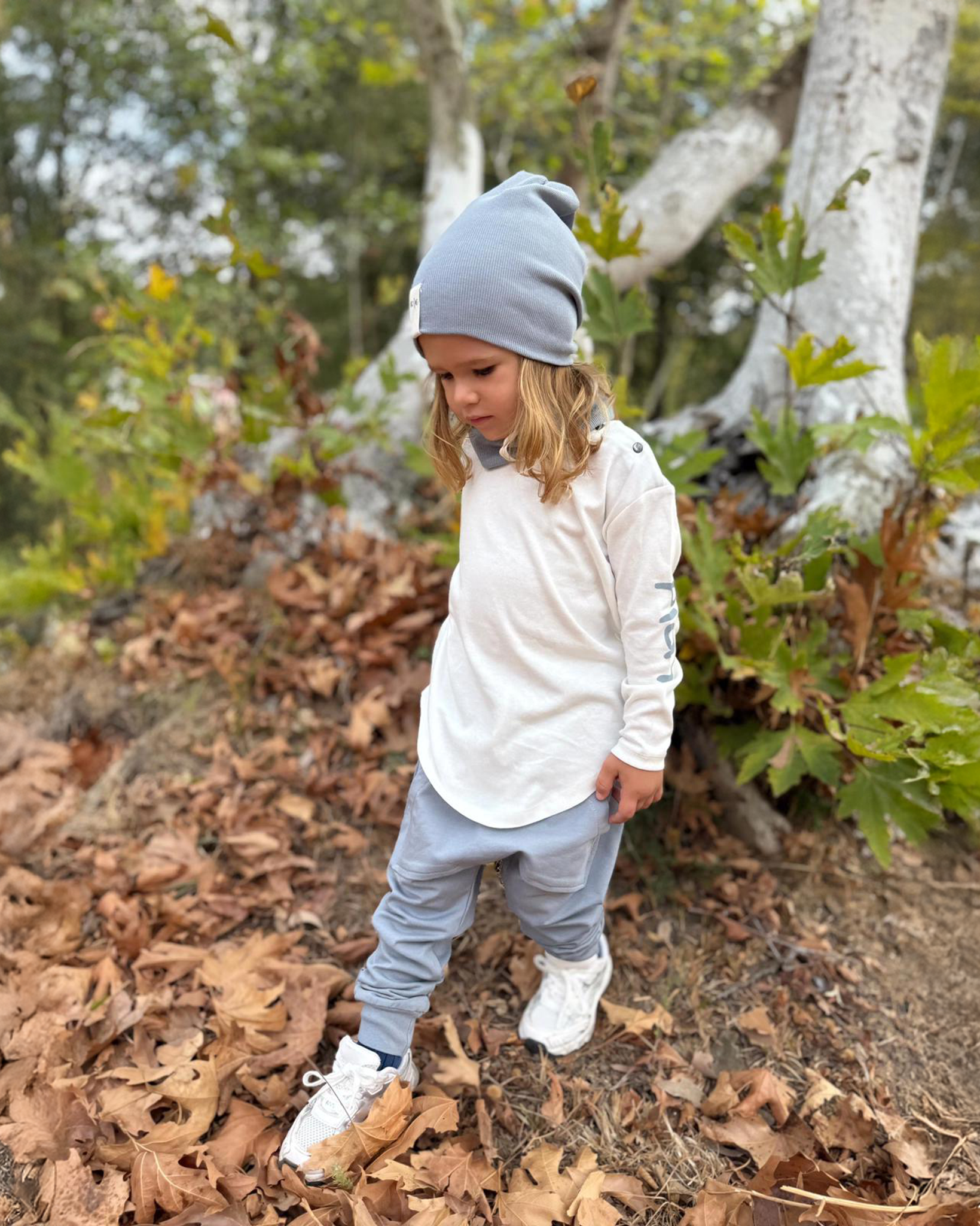 Child in a forest setting wearing a white jacket and gray beanie.