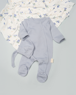 Light blue baby romper with footies on a gray surface with a floral blanket in the background