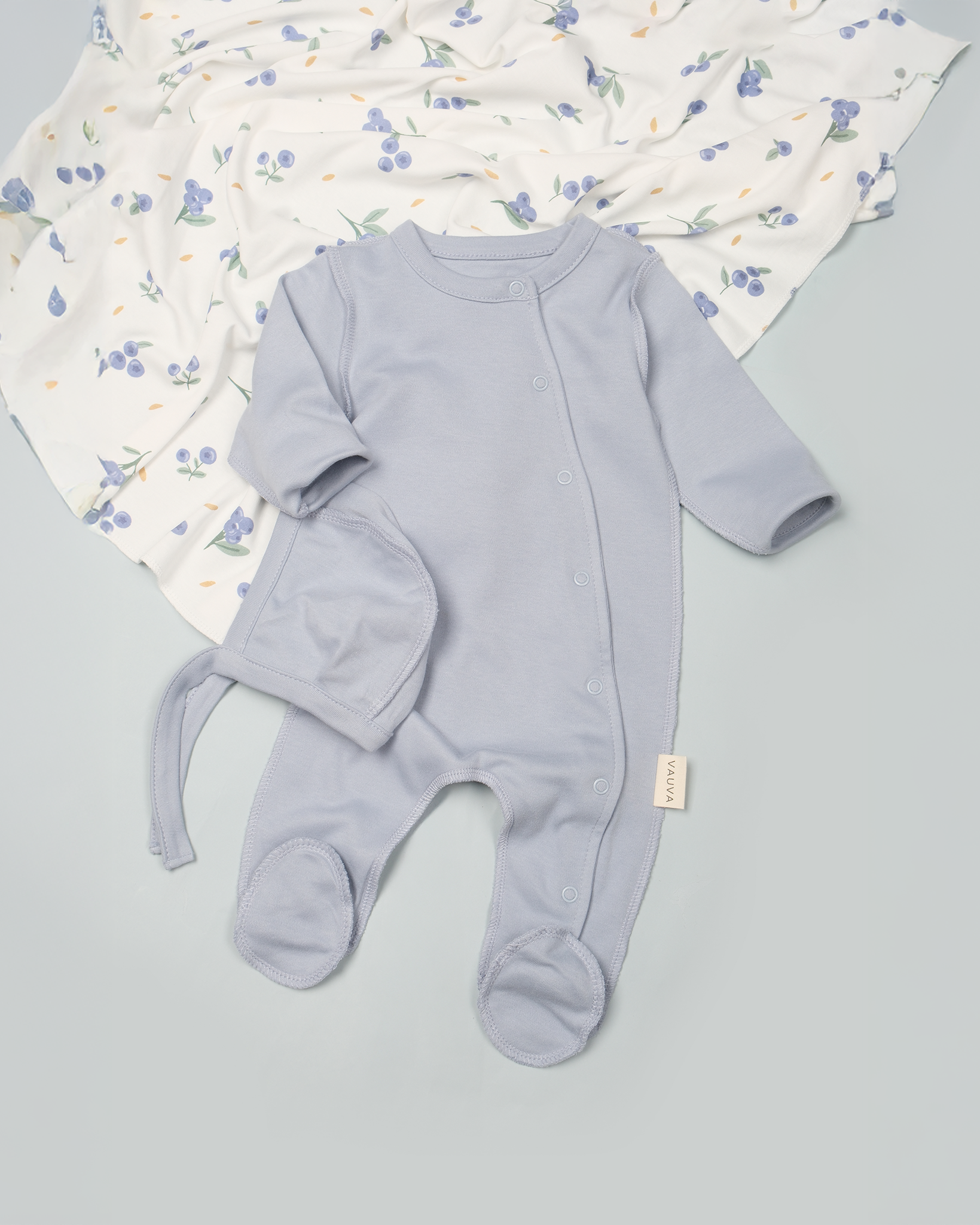 Light blue baby romper with footies on a gray surface with a floral blanket in the background