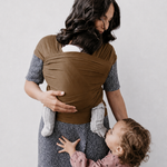 Nënë me baby wrap kafe rreth trupit, fëmija e vogël duke iu afruar