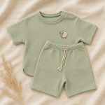 Green baby outfit with shorts and t-shirt on a beige background