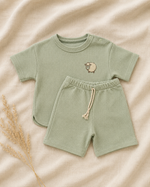 Green baby outfit with shorts and t-shirt on a beige background