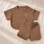 Brown baby outfit with shirt and shorts on a beige fabric background